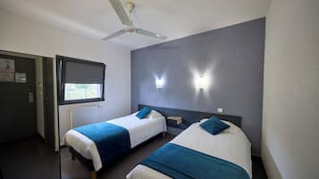 A hotel room with two beds, a ceiling fan, a window, and a wall-mounted nightstand.