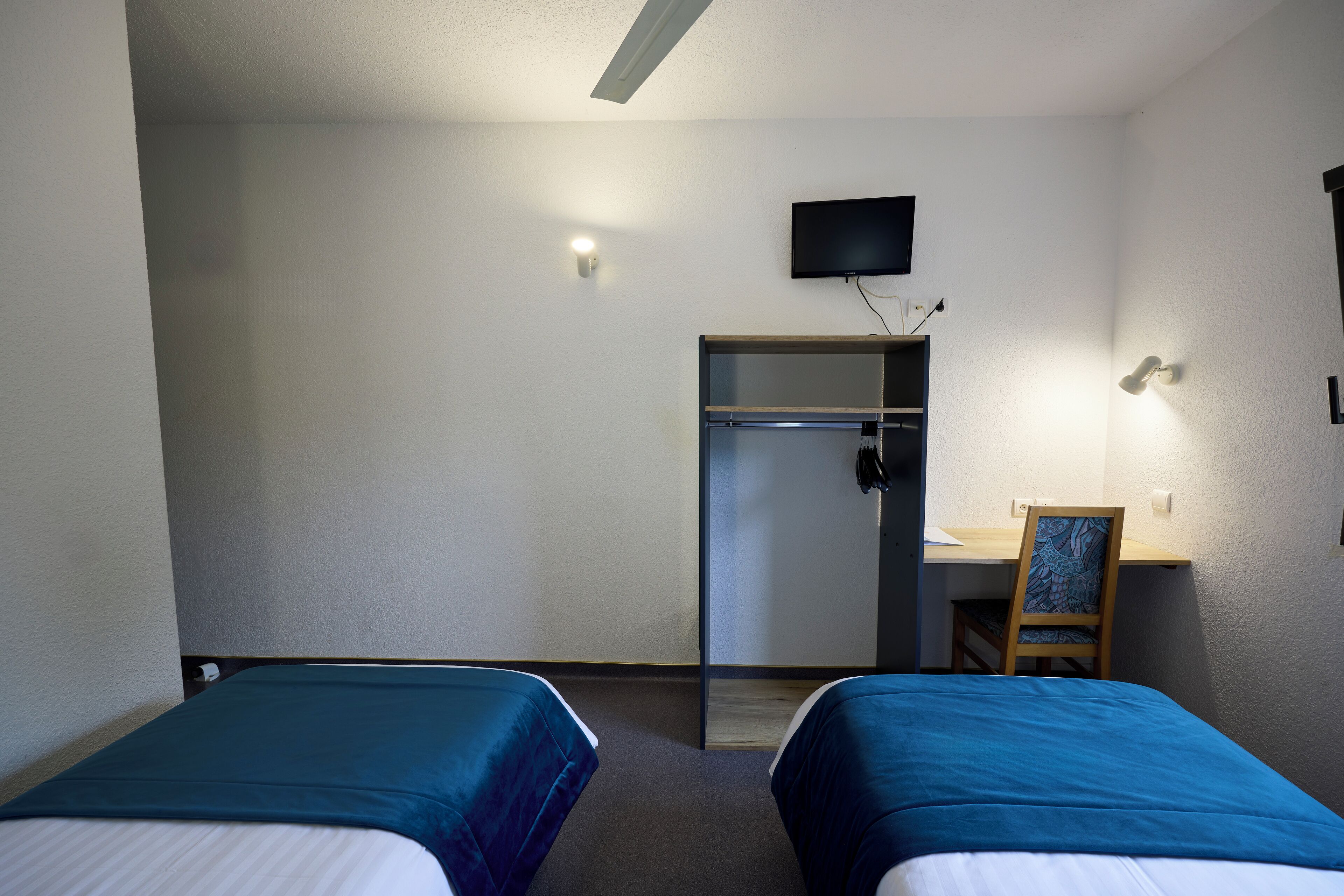 Une chambre d’hôtel avec deux lits, un bureau, une chaise, une télévision et une porte.