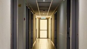 A long, narrow hallway with doors on both sides, a tiled floor, and a ceiling with recessed lighting. - Hôtel Eco (Banassac)