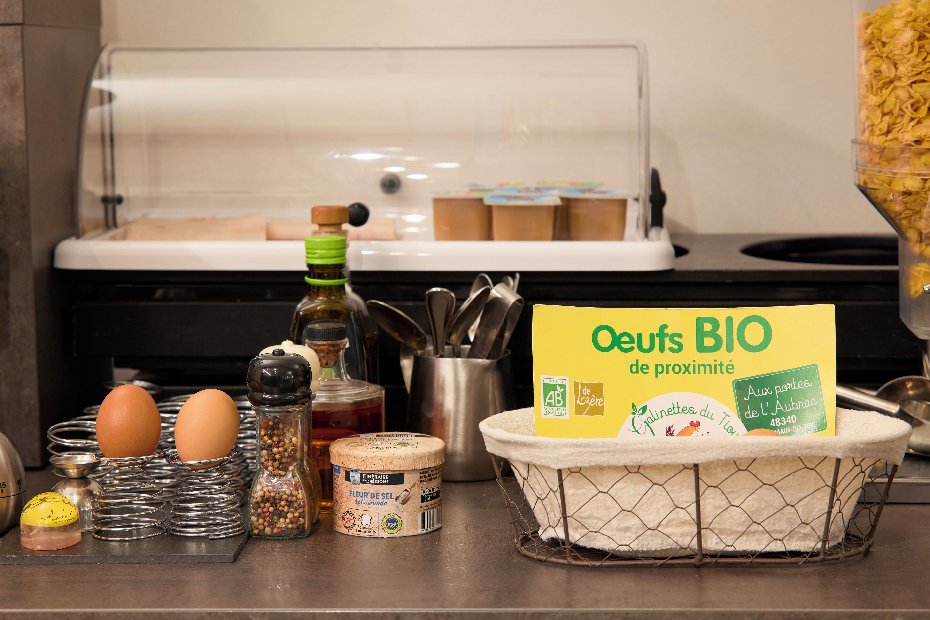A kitchen counter with eggs, a salt shaker, a pepper shaker, a bottle of oil, a jar of spices, a container of flour, and a basket of bread.