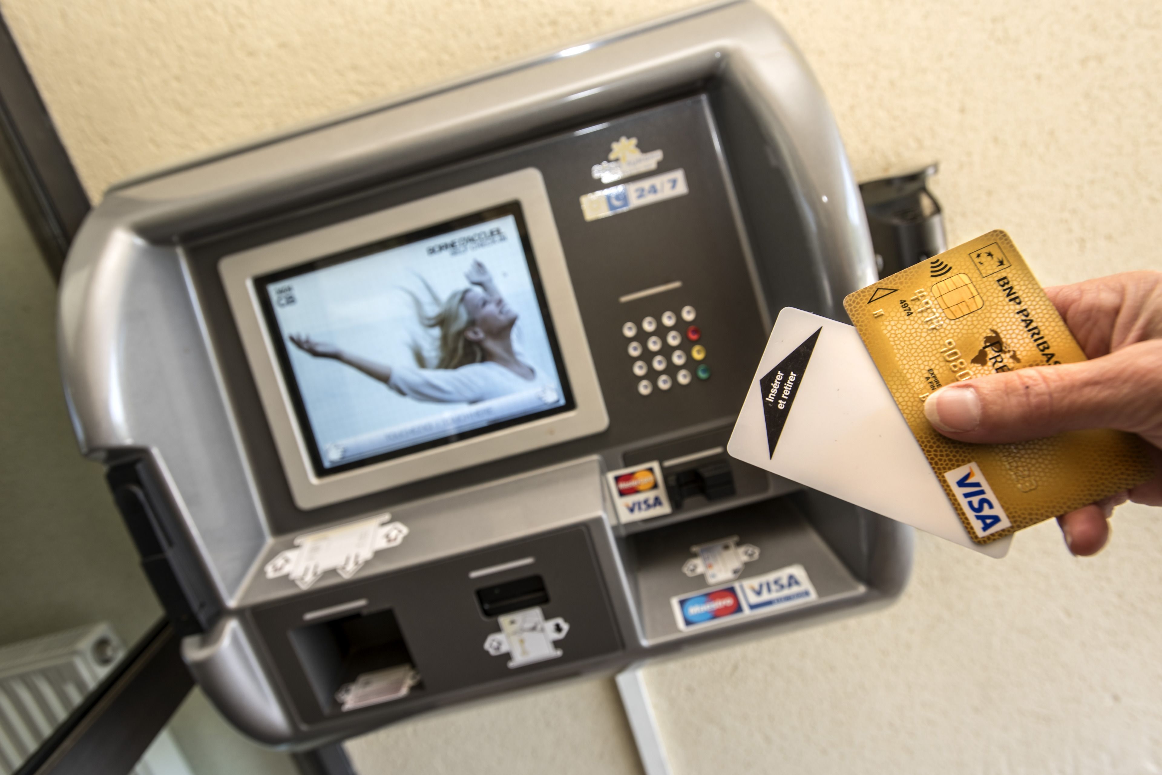 A payment terminal with a screen displaying a movie, Visa and Mastercard logos, and a hand holding a Visa card.