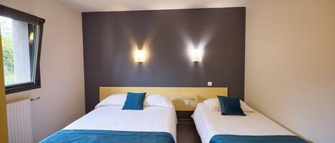Habitación de hotel con dos camas, cada una con colcha azul, ropa de cama blanca y dos lámparas fijadas a la pared.