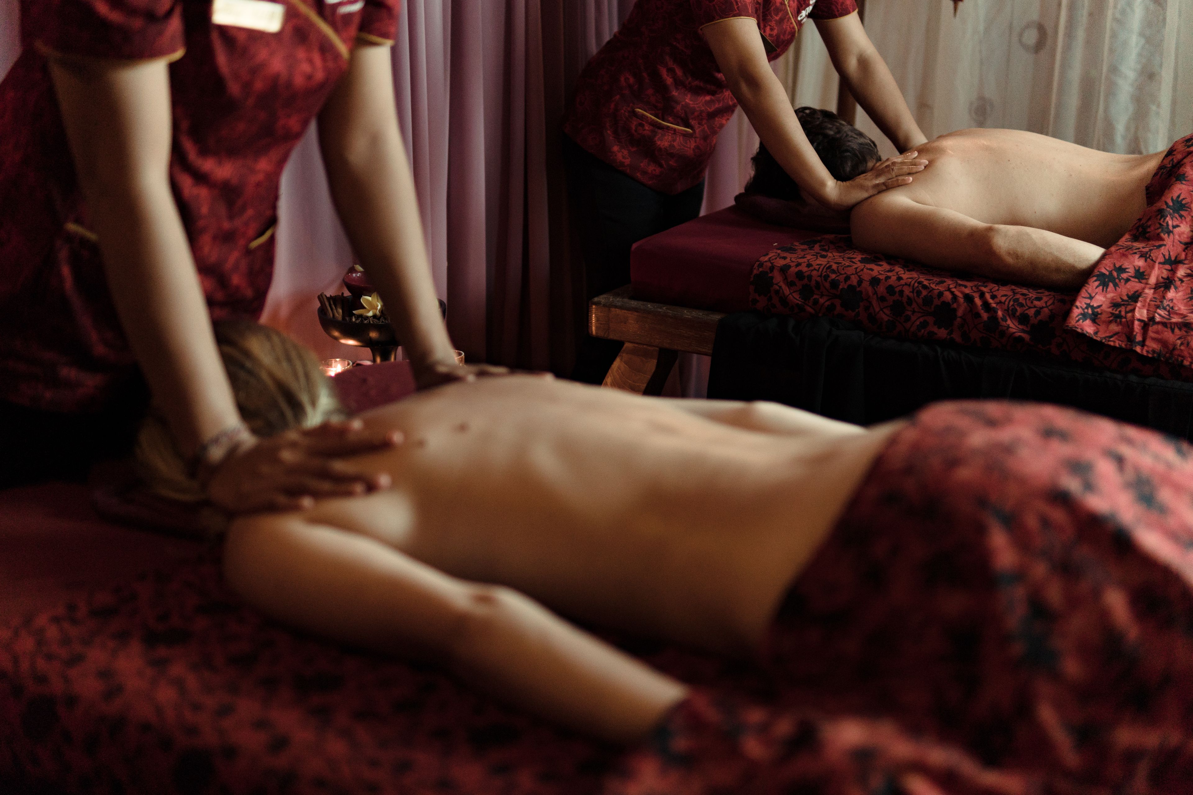 A massage therapy session in a room with a wooden massage table, a red patterned bed, and a curtain in the background.