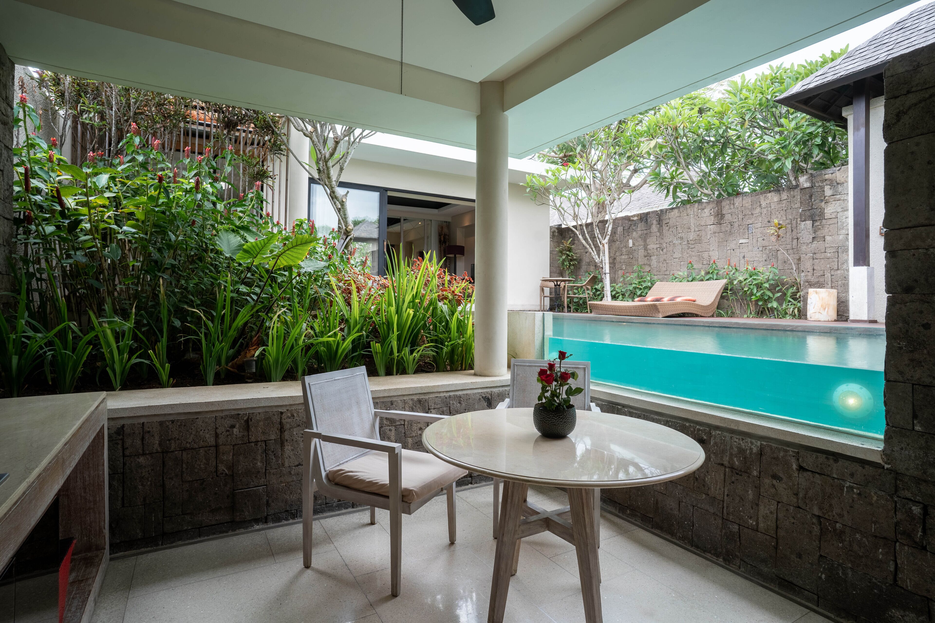 Eine Terrasse mit rundem Tisch, zwei Stühlen, einem kleinen Pool und üppiger Bepflanzung.