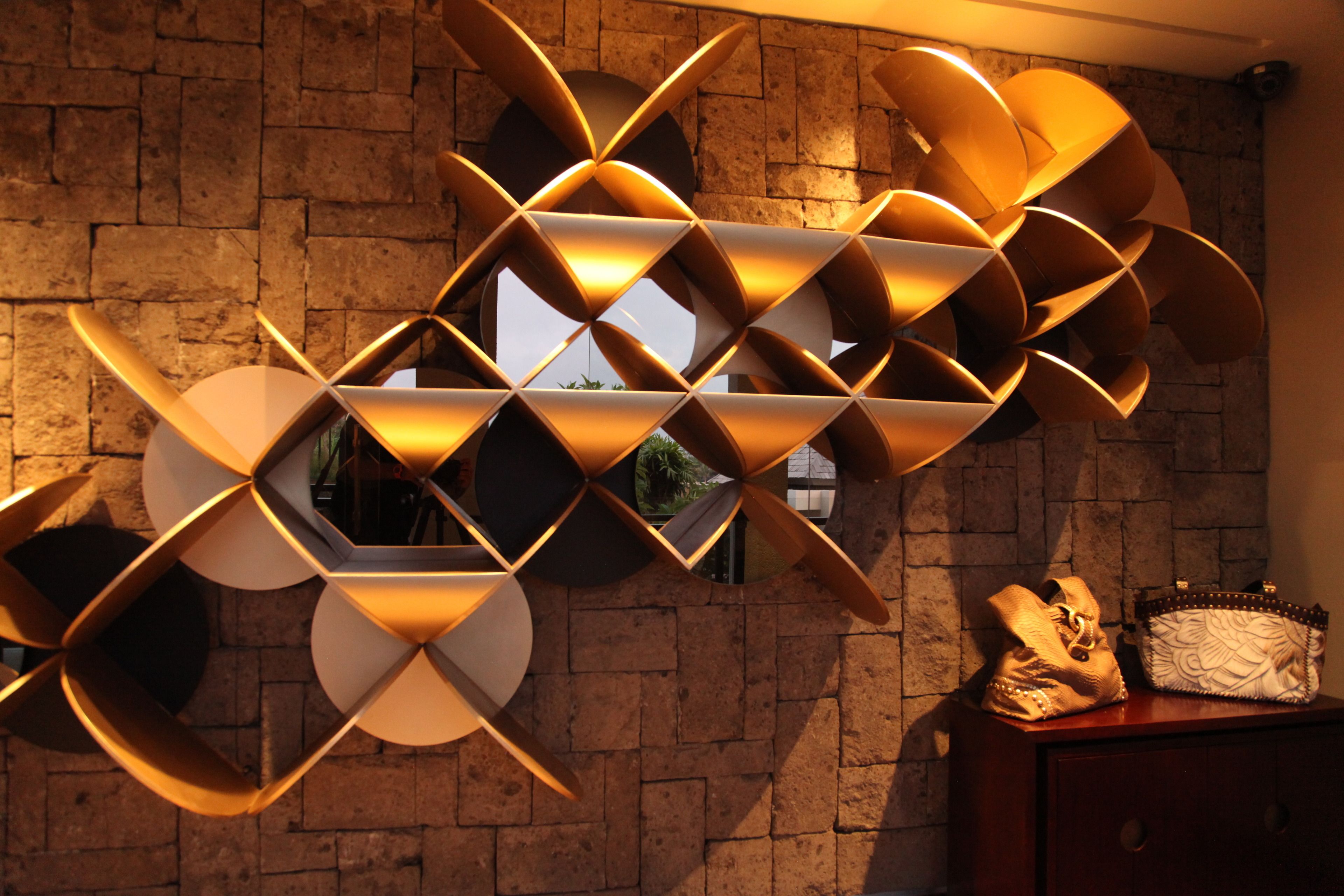 Eine geometrische Wandinstallation in einem Raum mit Backsteinwand und Fenster.