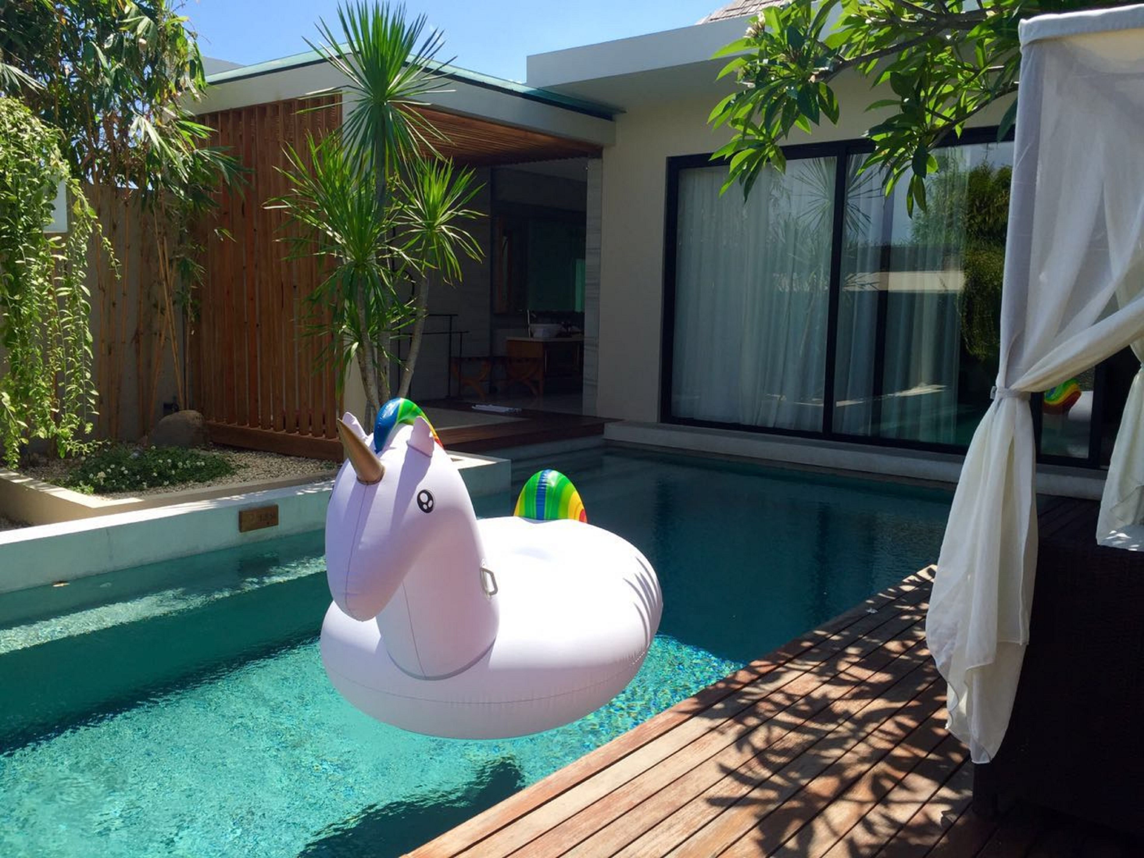 Una piscina moderna al aire libre con cubierta de madera y un flotador de unicornio inflable blanco.