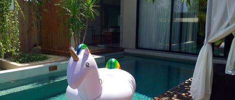 A modern outdoor swimming pool with a wooden deck and a white inflatable unicorn float.