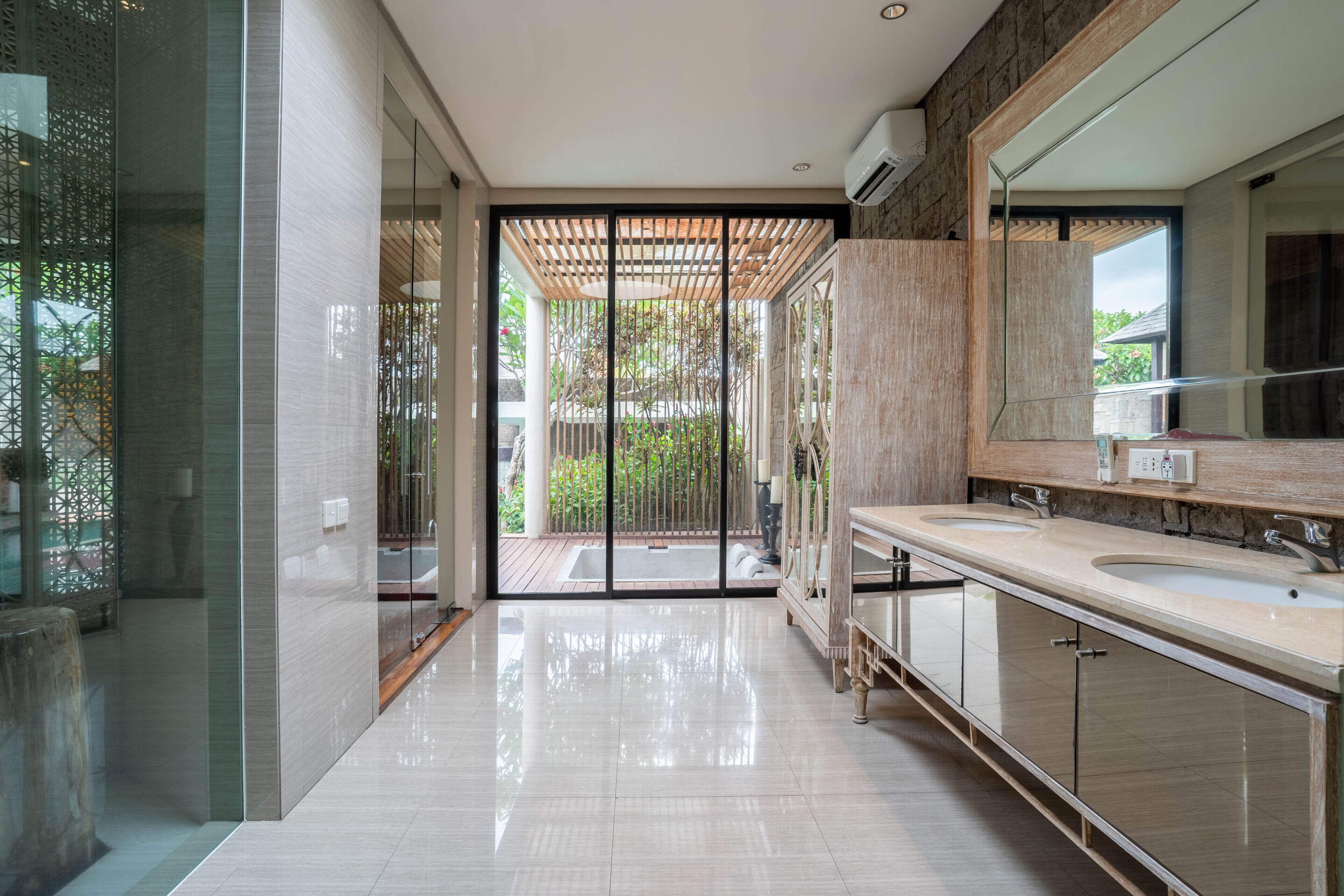 A modern bathroom with a large mirror, two sinks, and a glass door leading to an outdoor area.