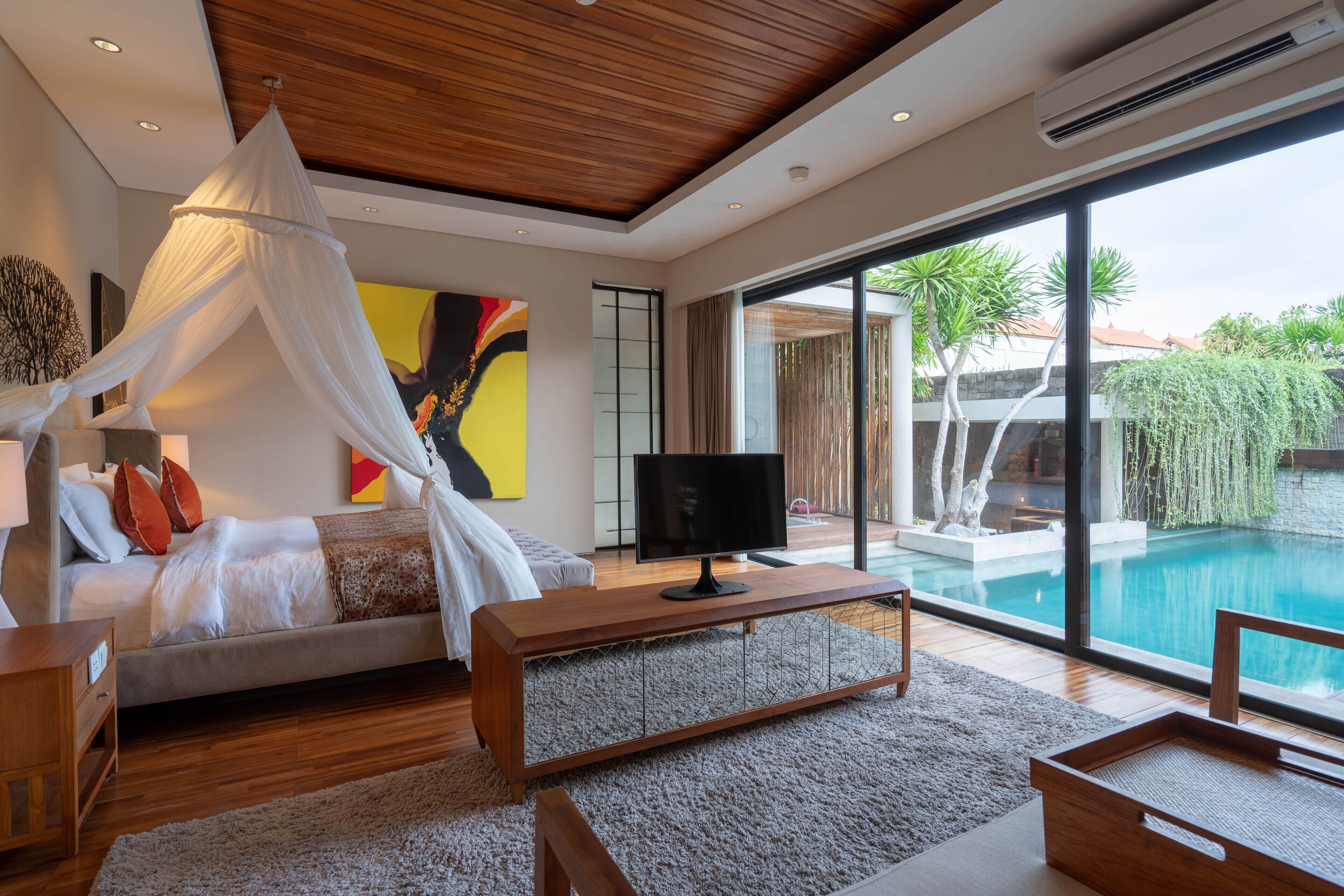 A modern bedroom with a bed, TV, and a view of a swimming pool.