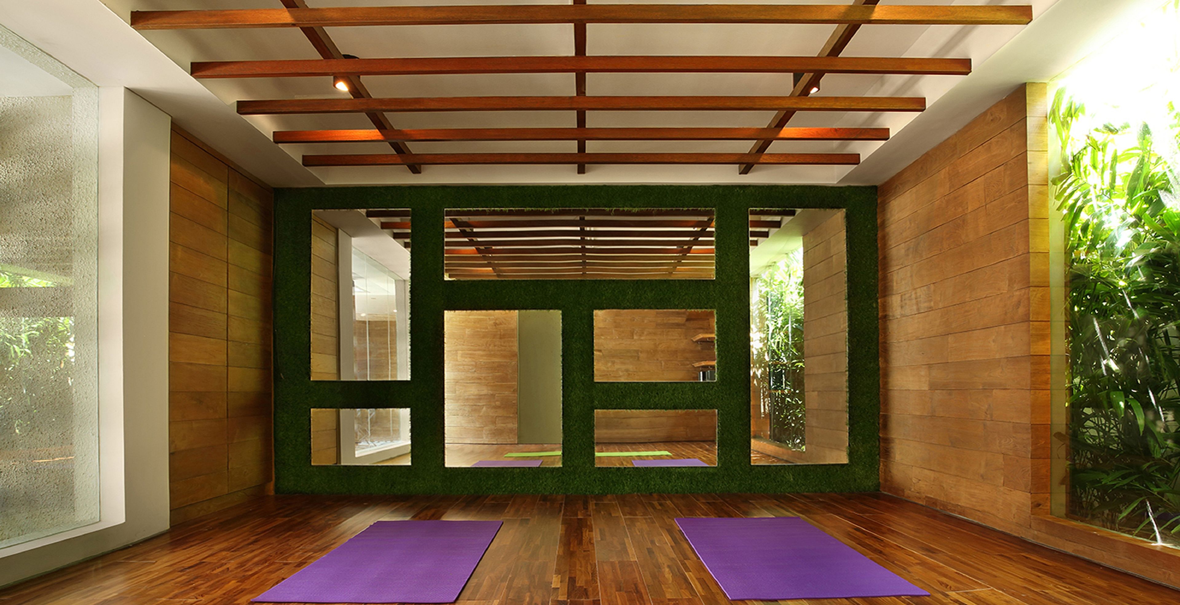 Ein Zimmer mit Holzboden, grünen Wänden und einer Decke mit Holzbalken. Auf dem Boden liegen zwei violette Yogamatten.