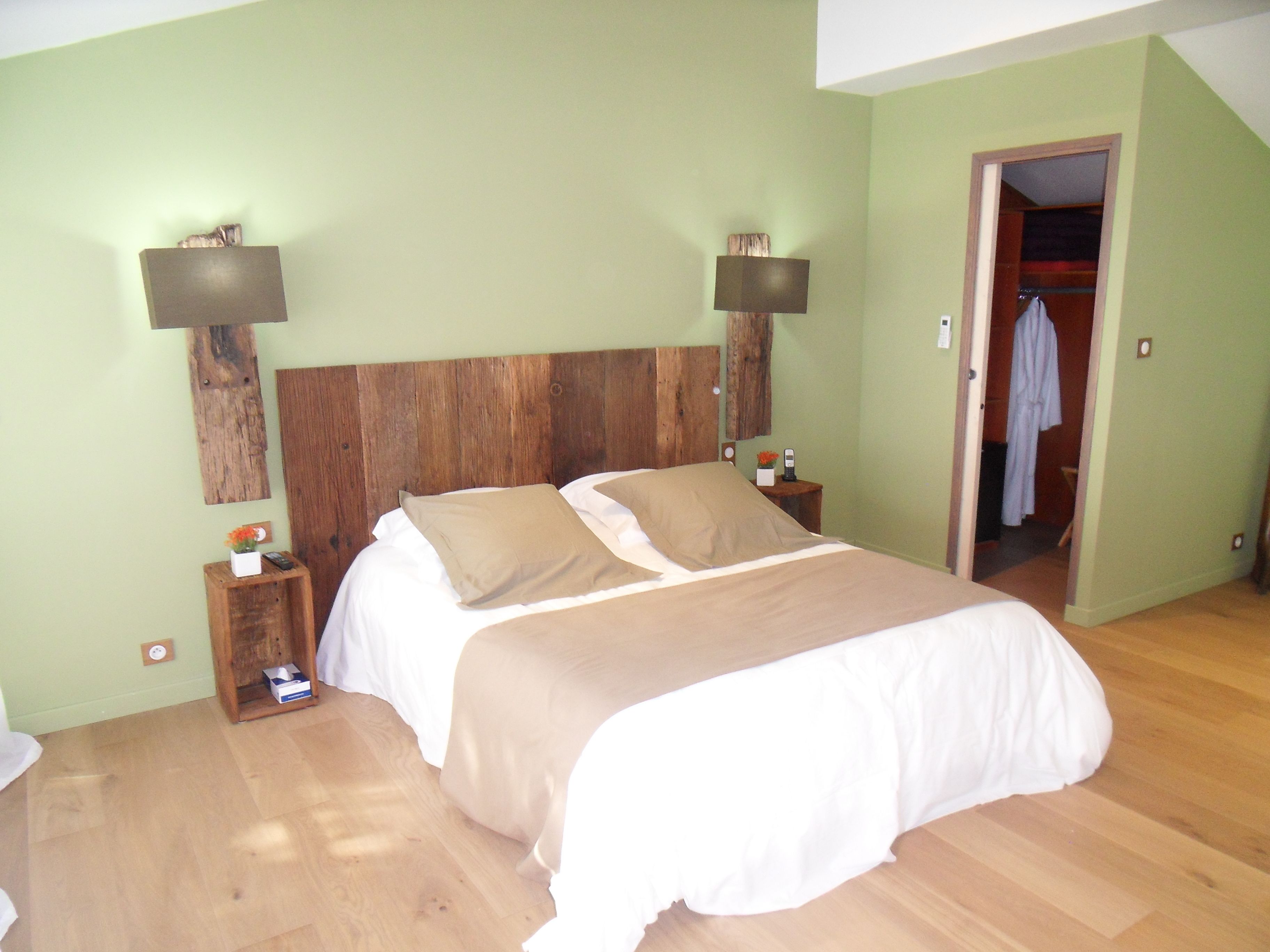 A bedroom with a wooden headboard, two bedside tables, a bed with white and beige bedding, and a wooden floor.