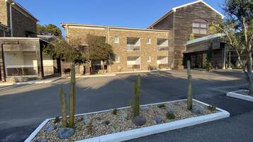 A multi-story building with a stone facade, multiple balconies, and a parking lot with a cactus garden.