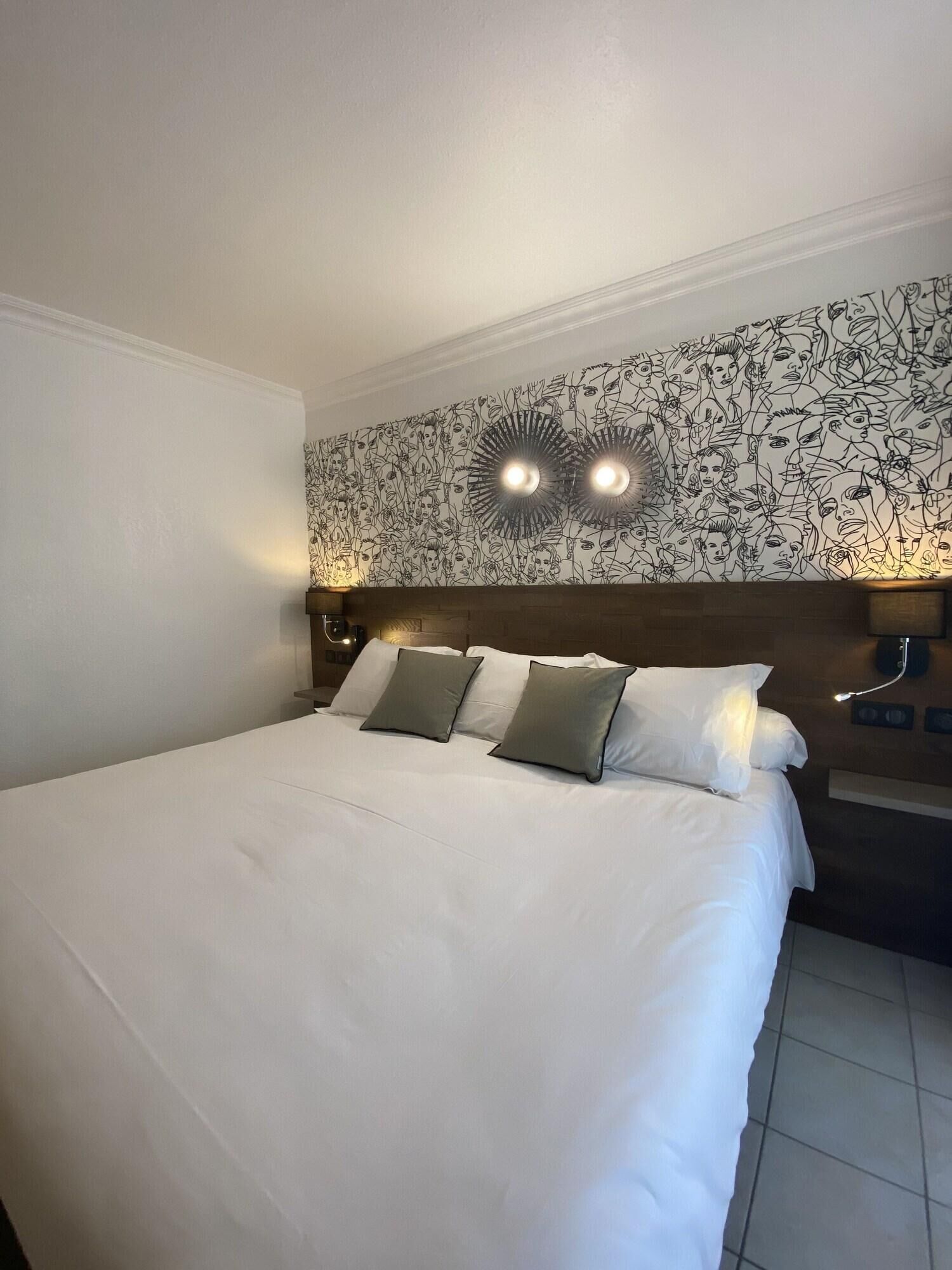 Una camera d'albergo con un letto grande, due lampade sui comodini, una testiera con motivo floreale e una parete con un disegno circolare.
