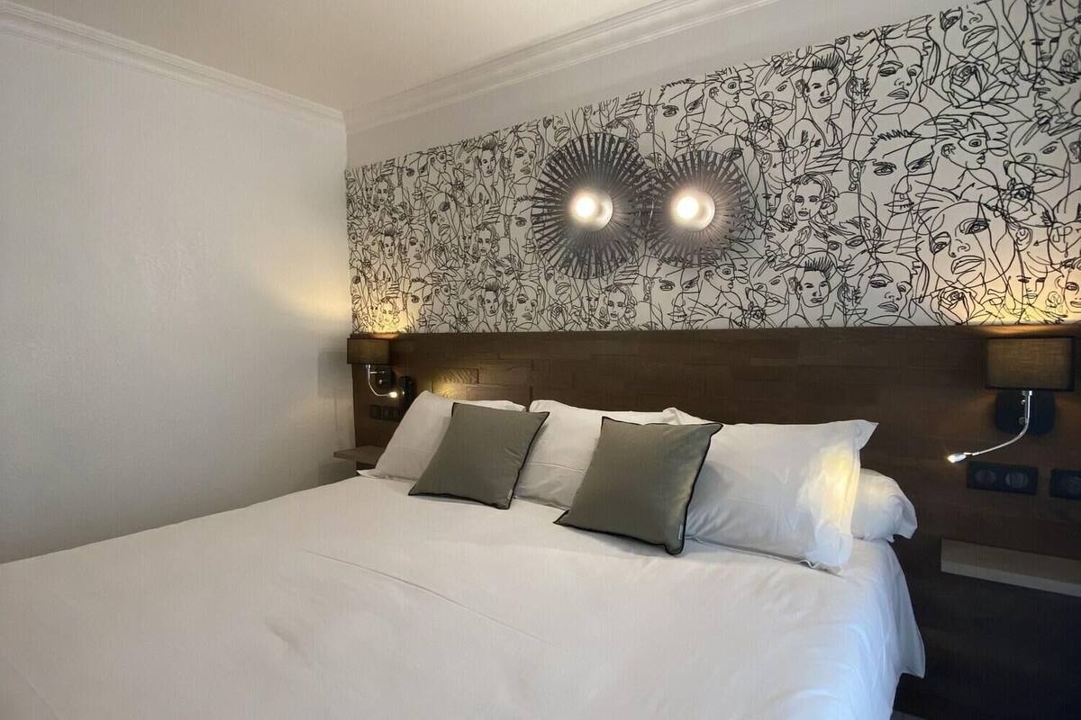 Hotellihuone, jossa on suuri sänky, kaksi yöpöytävalaisinta ja kukallinen tapetti.