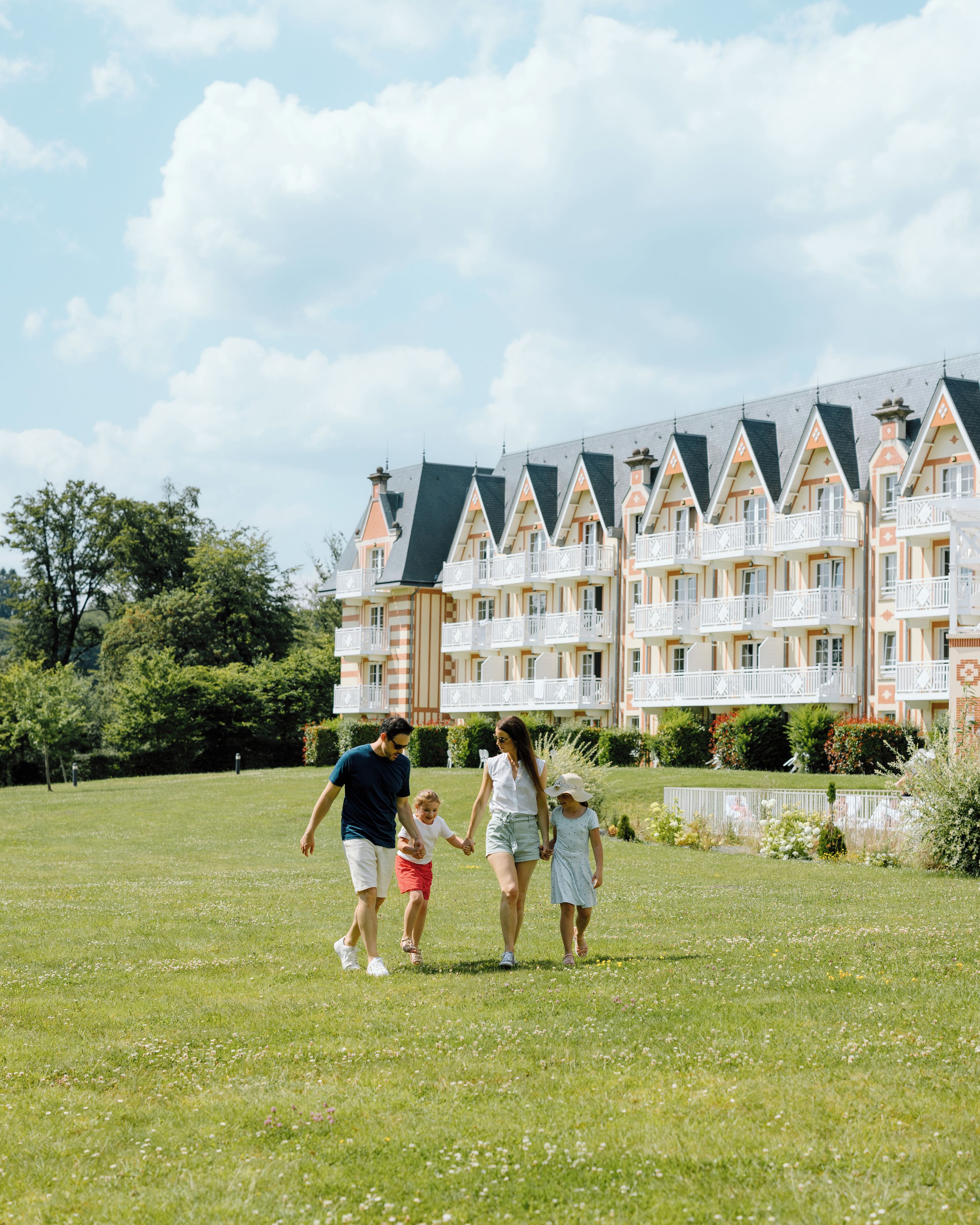 A family walking on a grassy lawn with a row of multi-story buildings in the background.
