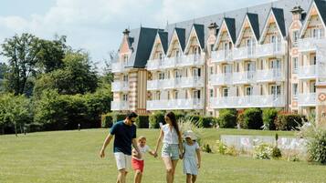 A family walking on a grassy lawn with a row of multi-story buildings in the background.