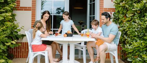 A family dining at an outdoor table with a brick wall and greenery in the background.