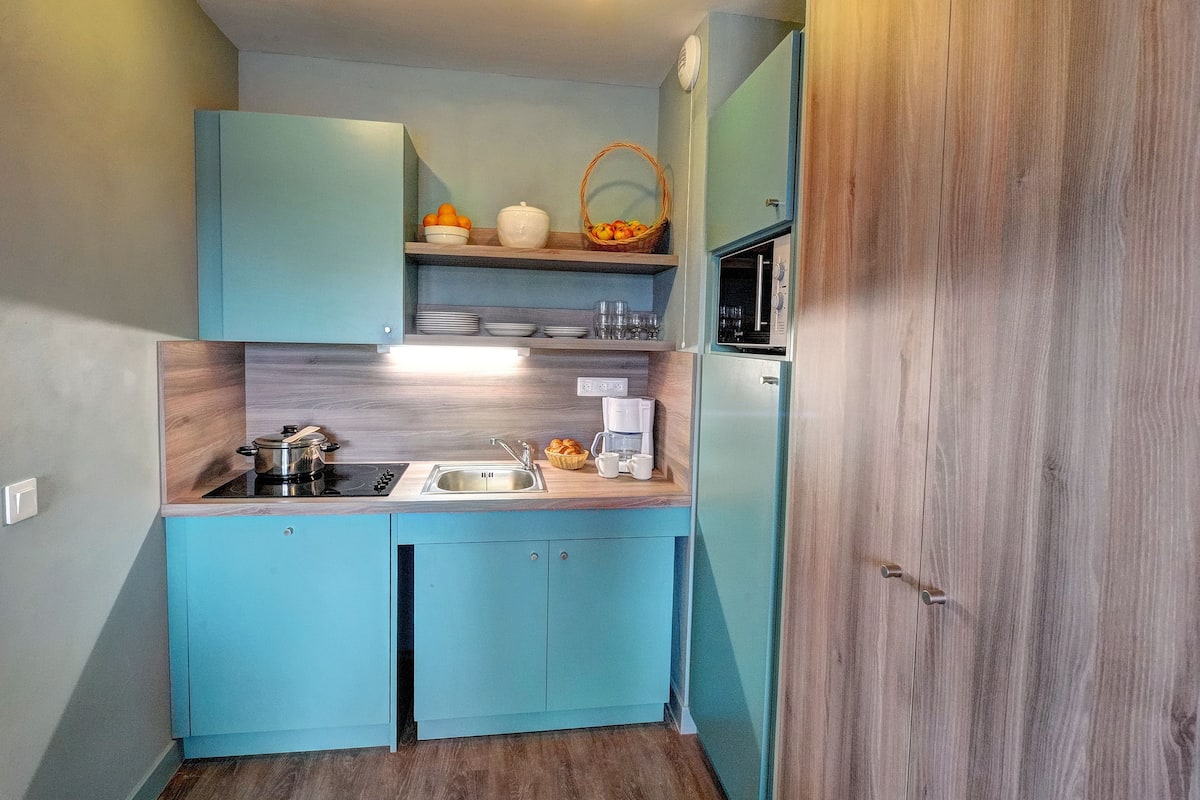 A compact kitchen with teal cabinetry, a built-in stove, a sink, and a microwave.