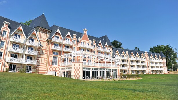 Un hotel grande de varios pisos con un estilo arquitectónico distintivo, que presenta colores rojo y beige, varios balcones y un amplio jardín.