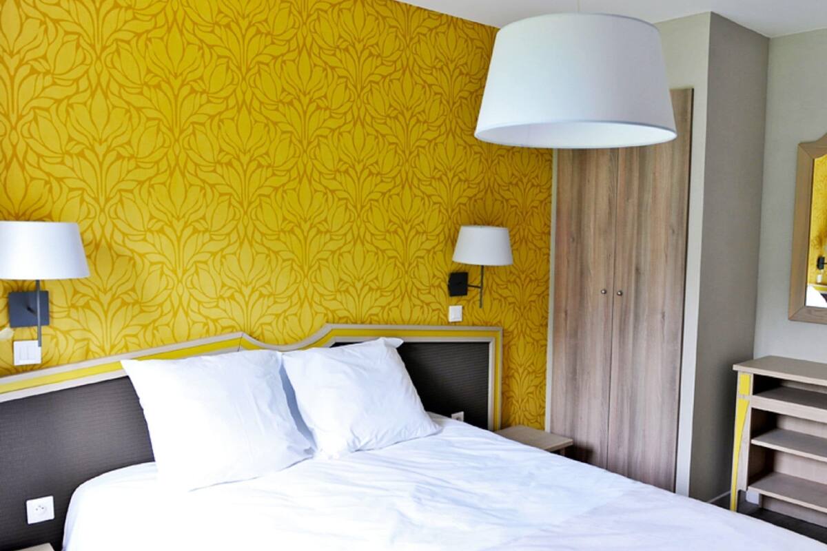 A hotel room with a bed, two bedside lamps, a wardrobe, and a mirror on the wall.