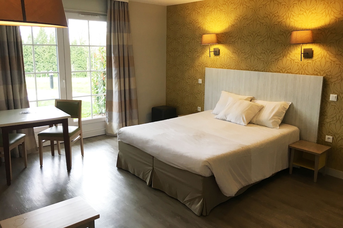 A hotel room with a bed, a desk, a chair, and two wall-mounted lamps.