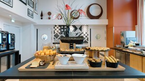 Una mesa de bufé con diversos alimentos, un jarrón con flores y una cafetera.
