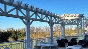 Un patio al aire libre con mobiliario de mimbre blanco y una estructura de pérgola.