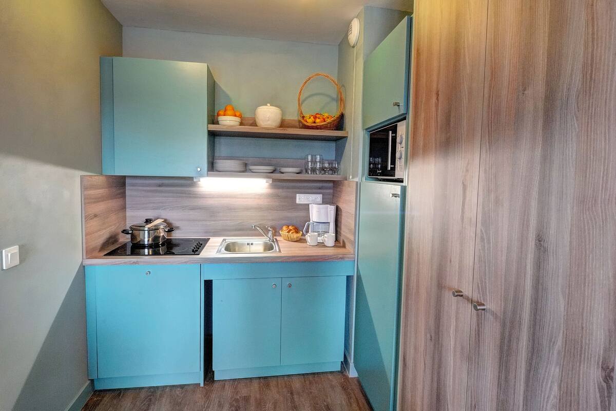 A compact kitchen with teal cabinetry, a built-in stove, a sink, and a microwave.