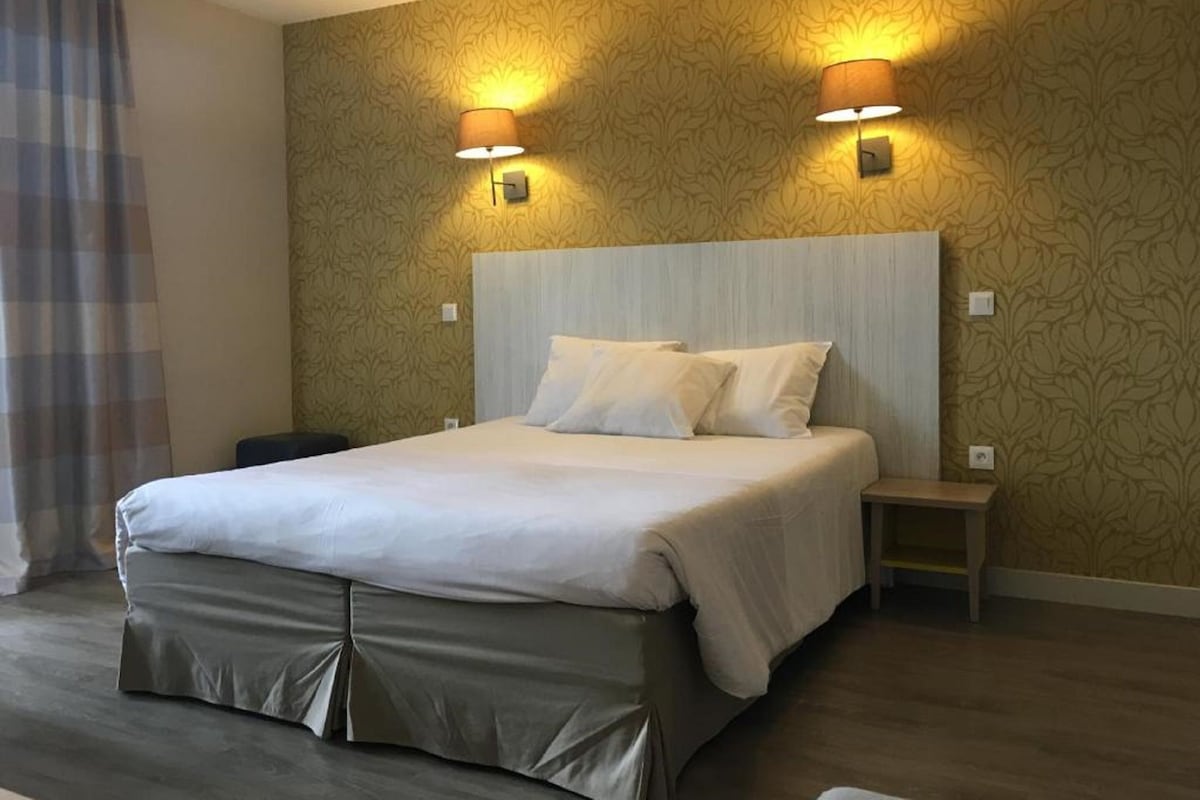 A hotel room with a large bed, two bedside lamps, a nightstand, and a patterned wallpaper.