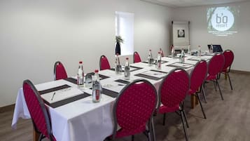 A conference room with a long table, red chairs, and a white tablecloth. There are water bottles and a laptop on the table.