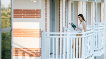 A person standing on a balcony with white railings, reading a book.