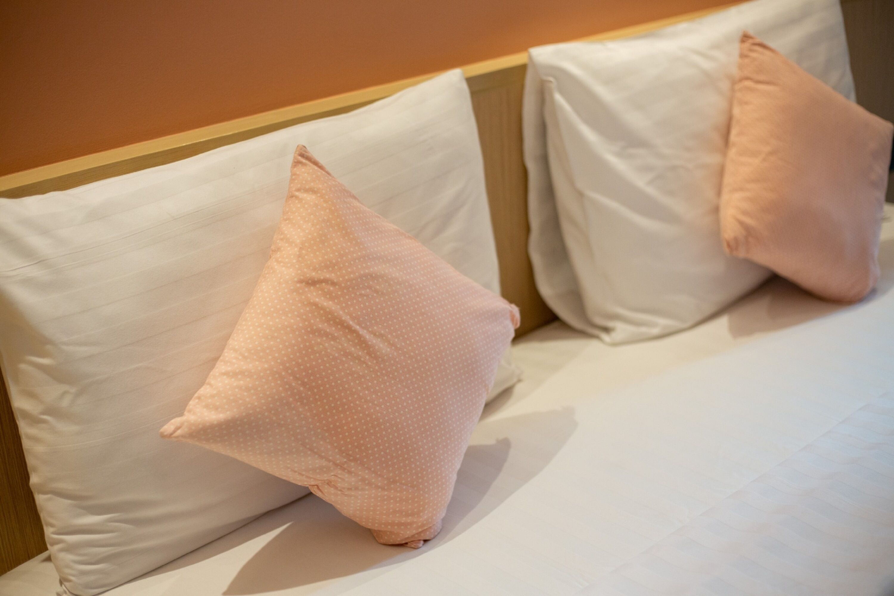 A bed with white sheets and two pink pillows.