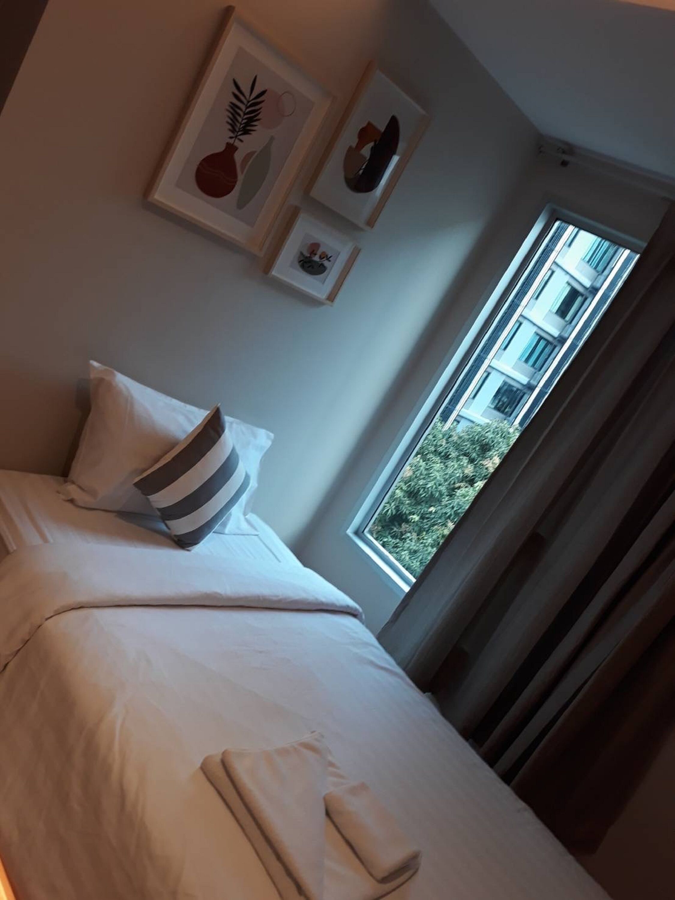 A hotel room with a bed, pillows, a window with curtains, and framed artwork on the wall.