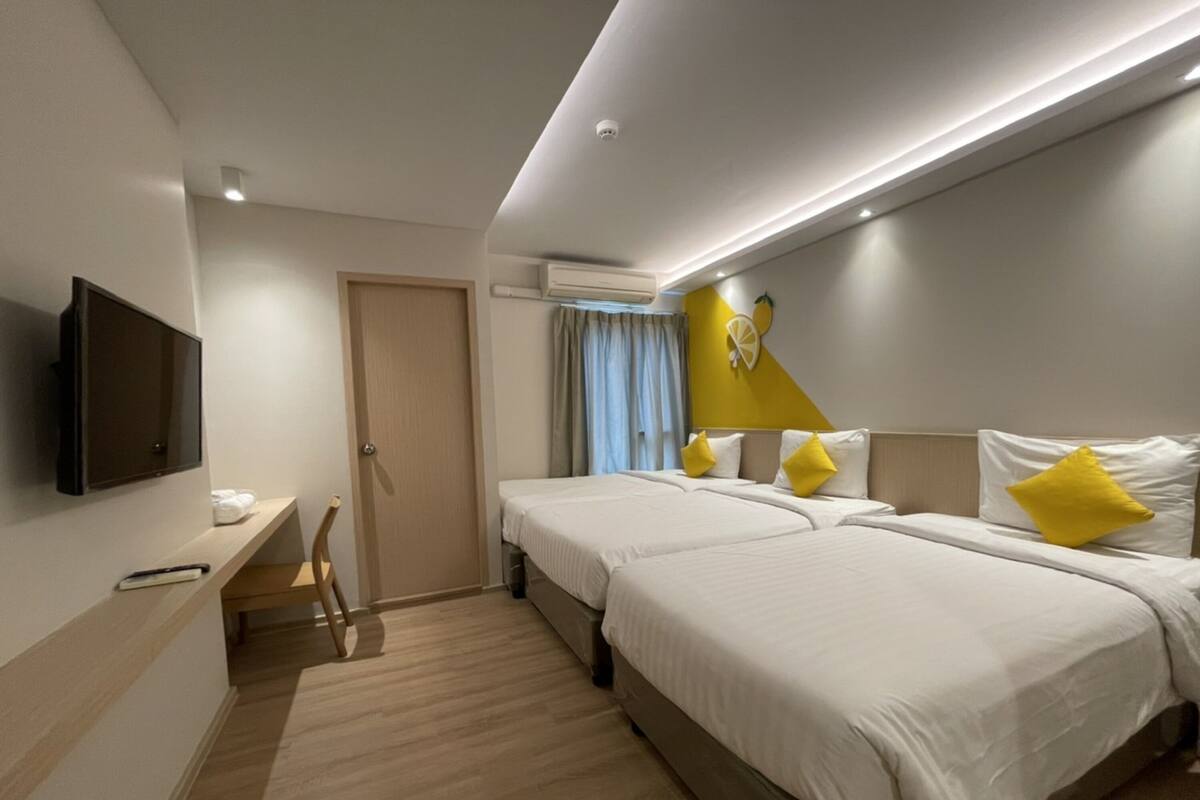 A hotel room with two beds, a desk, a TV, and an air conditioning unit.