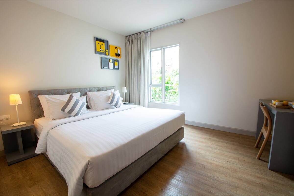 A modern bedroom with a large bed, bedside tables, a desk, and a window with curtains.