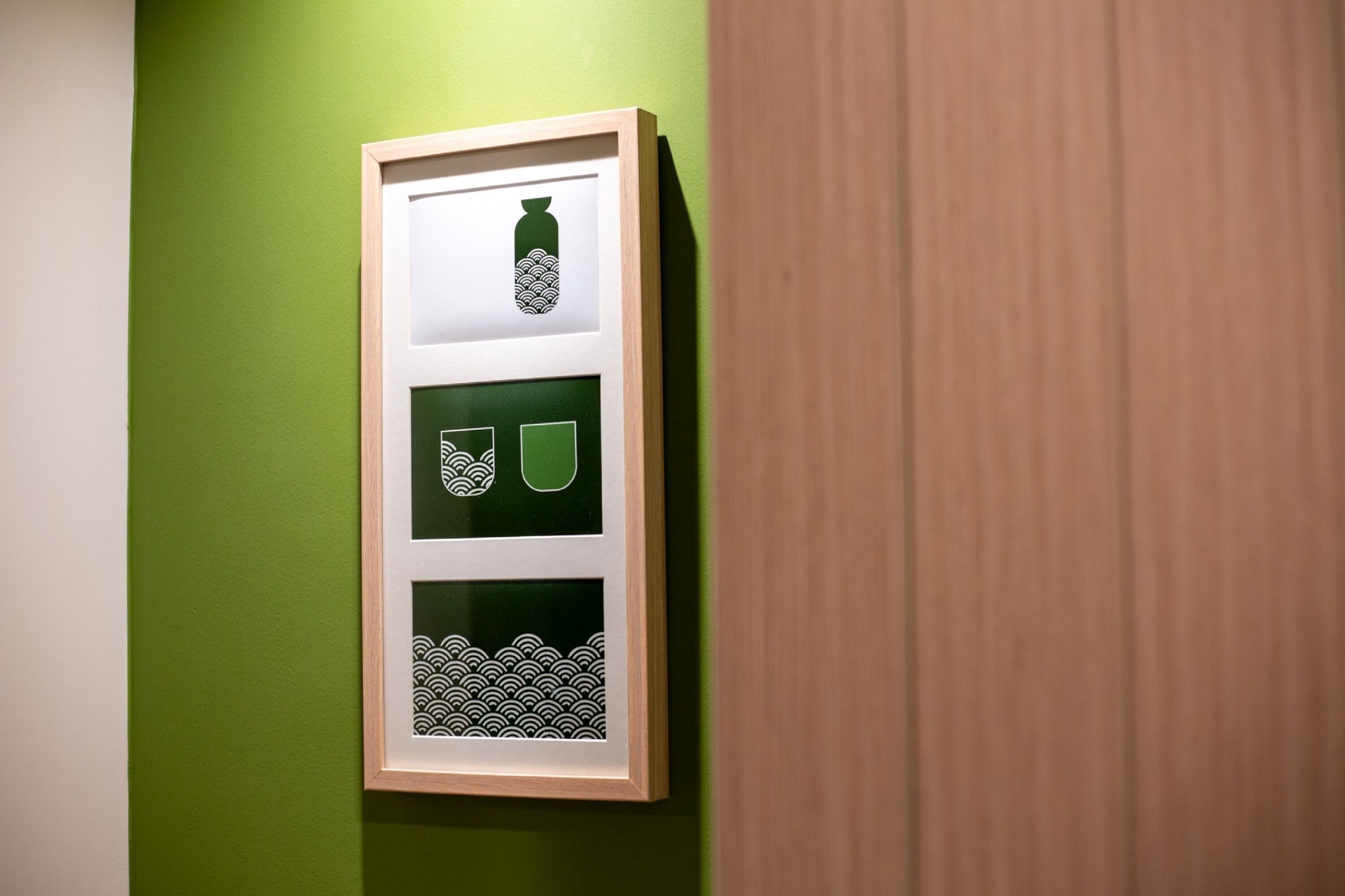 Een lijst met een kunstwerk bestaande uit drie panelen, hangend aan een groene muur.