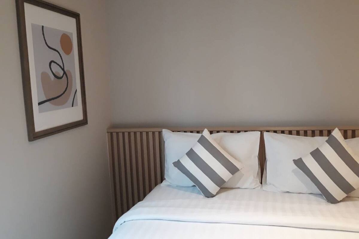 A neatly made bed with striped pillows, a framed abstract artwork on the wall, and a wooden headboard.