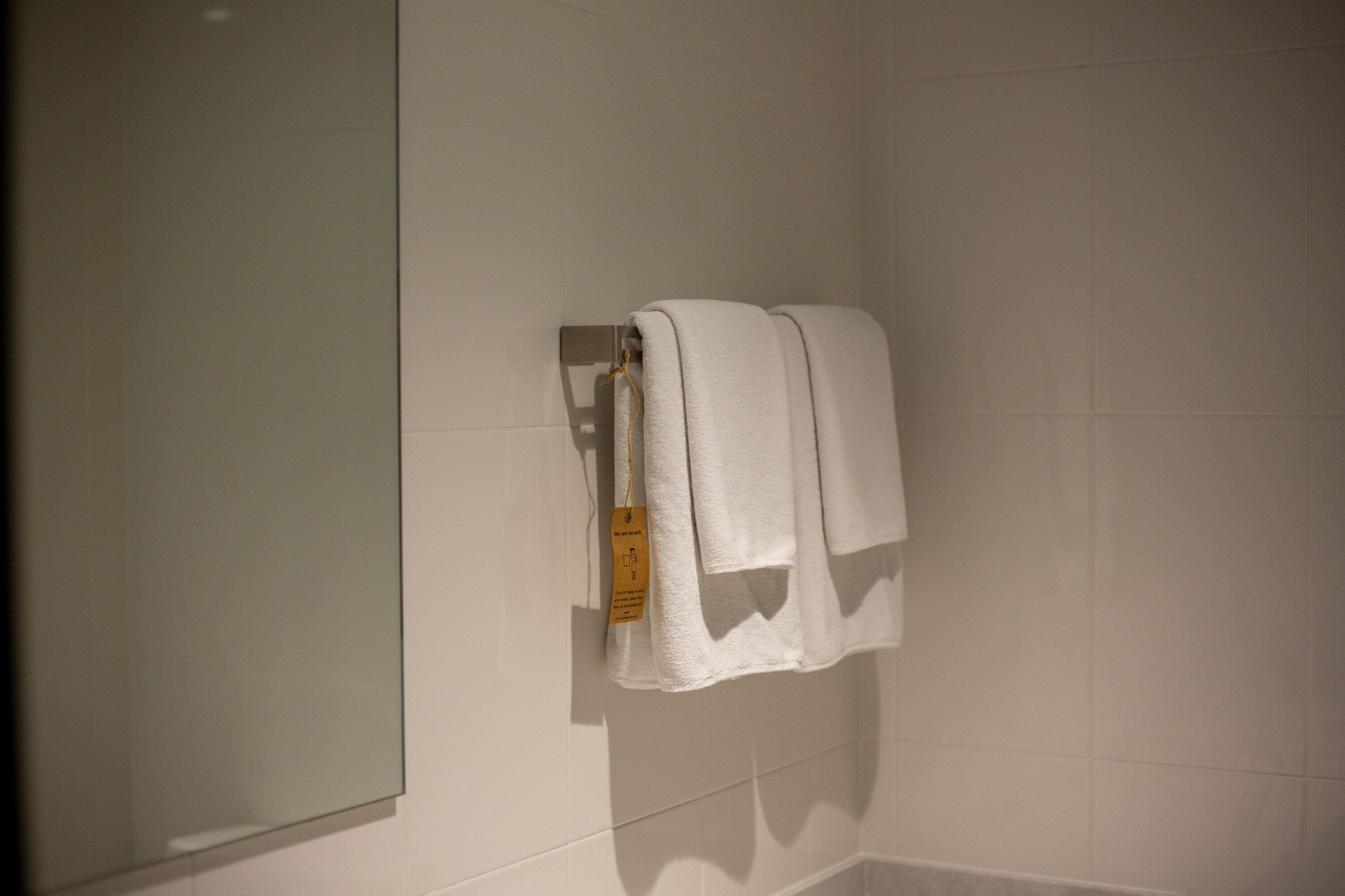 A bathroom with white tiled walls, a glass shower enclosure, and two white towels hanging on a towel rack.