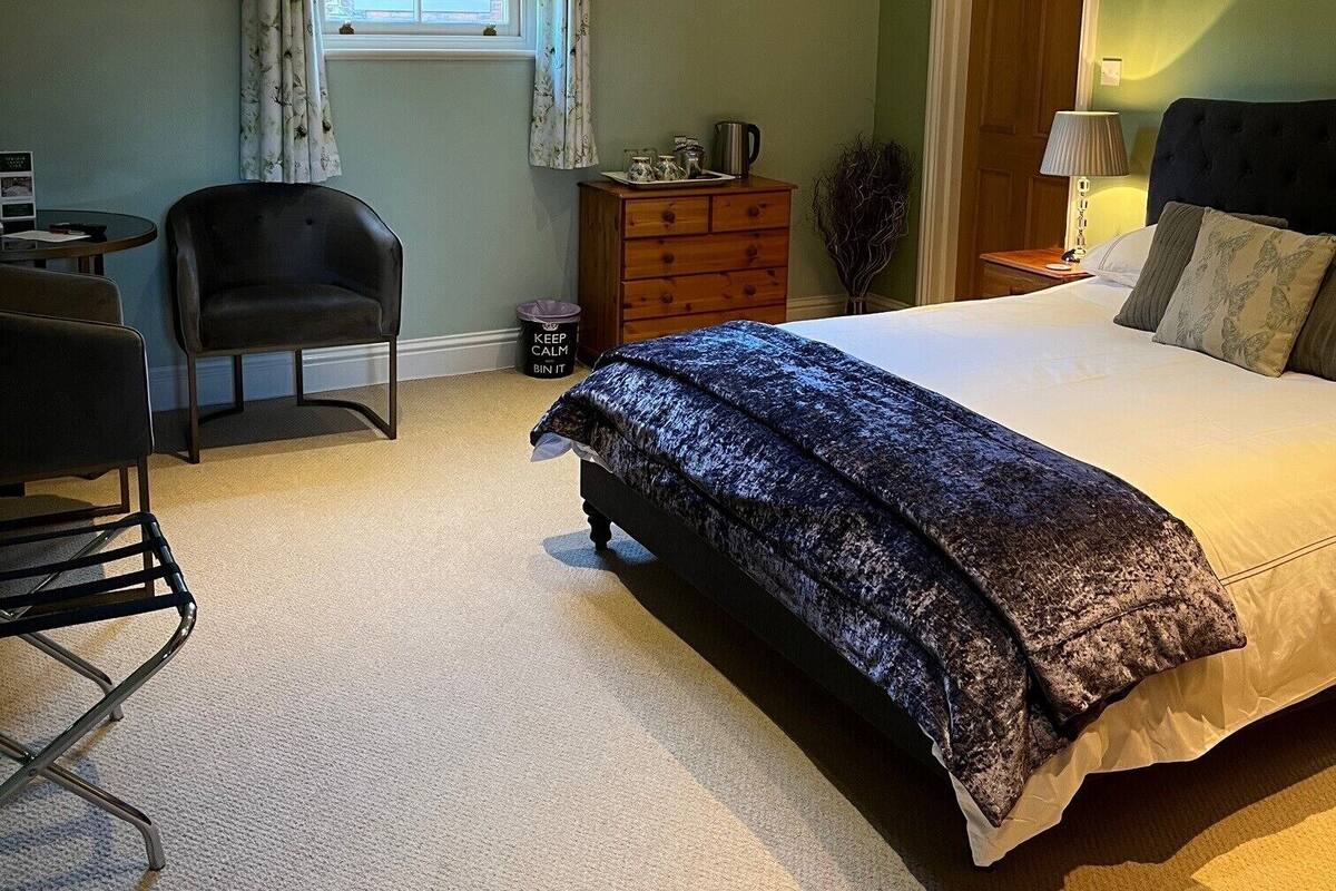 Un dormitorio con una cama, una silla, un tocador, una lámpara y una ventana.