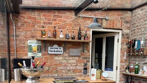 Un área de bar acogedora con pared de ladrillo, un cartel que da la bienvenida a visitantes a Yorkshire y una variedad de botellas en estanterías.