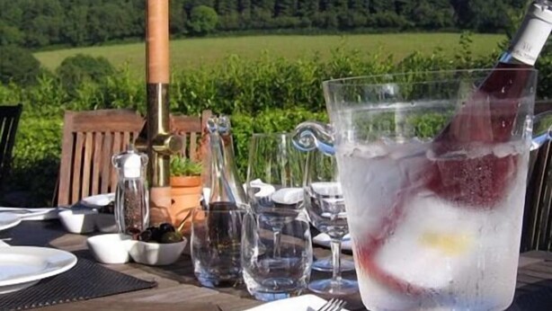 A table set outdoors with a glass of iced drink, a bottle, and a bowl of olives. - Plantation House Hotel (Ivybridge)