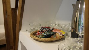 A breakfast setup with a basket of coffee pods, a coffee maker, and several glasses on a white countertop.