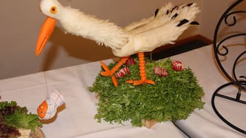 A table with a centerpiece featuring a bird sculpture with orange beak and feet, surrounded by green foliage and red and white striped decorations.