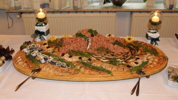 Ein großes, ovales Tablett mit verschiedenen Meeresfrüchten und Gemüse, begleitet von zwei Kerzen und zwei Löffeln auf einer weißen Tischdecke.