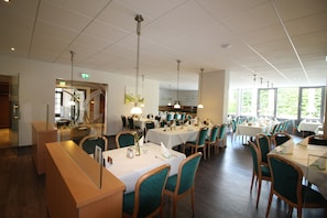 A restaurant with multiple tables and chairs, a reception desk, and a staircase leading to an upper level.