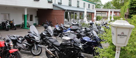 Varias motocicletas estacionadas frente a un edificio con toldo verde y un letrero que dice 'HOLSTEN Pilsener'.