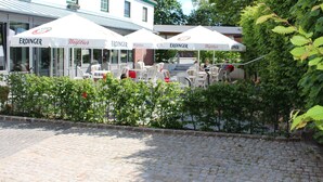Un patio con mesas al aire libre, sombrillas blancas y un edificio con la marca Erdinger.