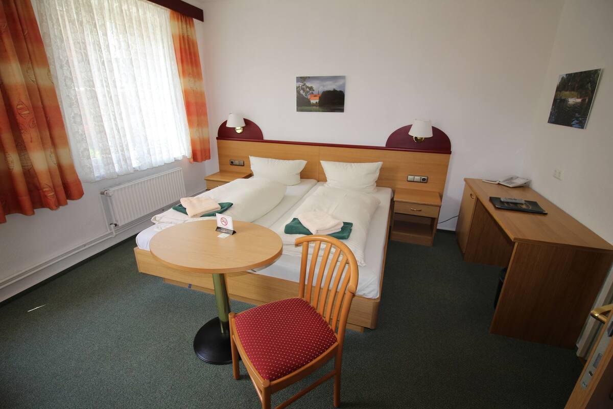 Ein Hotelzimmer mit Bett, Schreibtisch, Stuhl, rundem Tisch und einem Fenster mit Vorhängen.