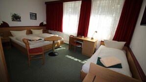 Habitación de hotel con dos camas, un escritorio y una silla. Se ven dos ventanas con cortinas rojas.
