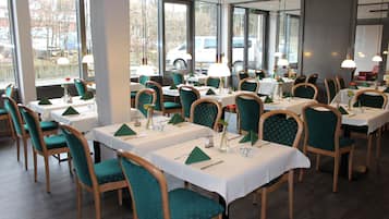 A restaurant with multiple tables and chairs, large windows, and a view of parked cars outside.